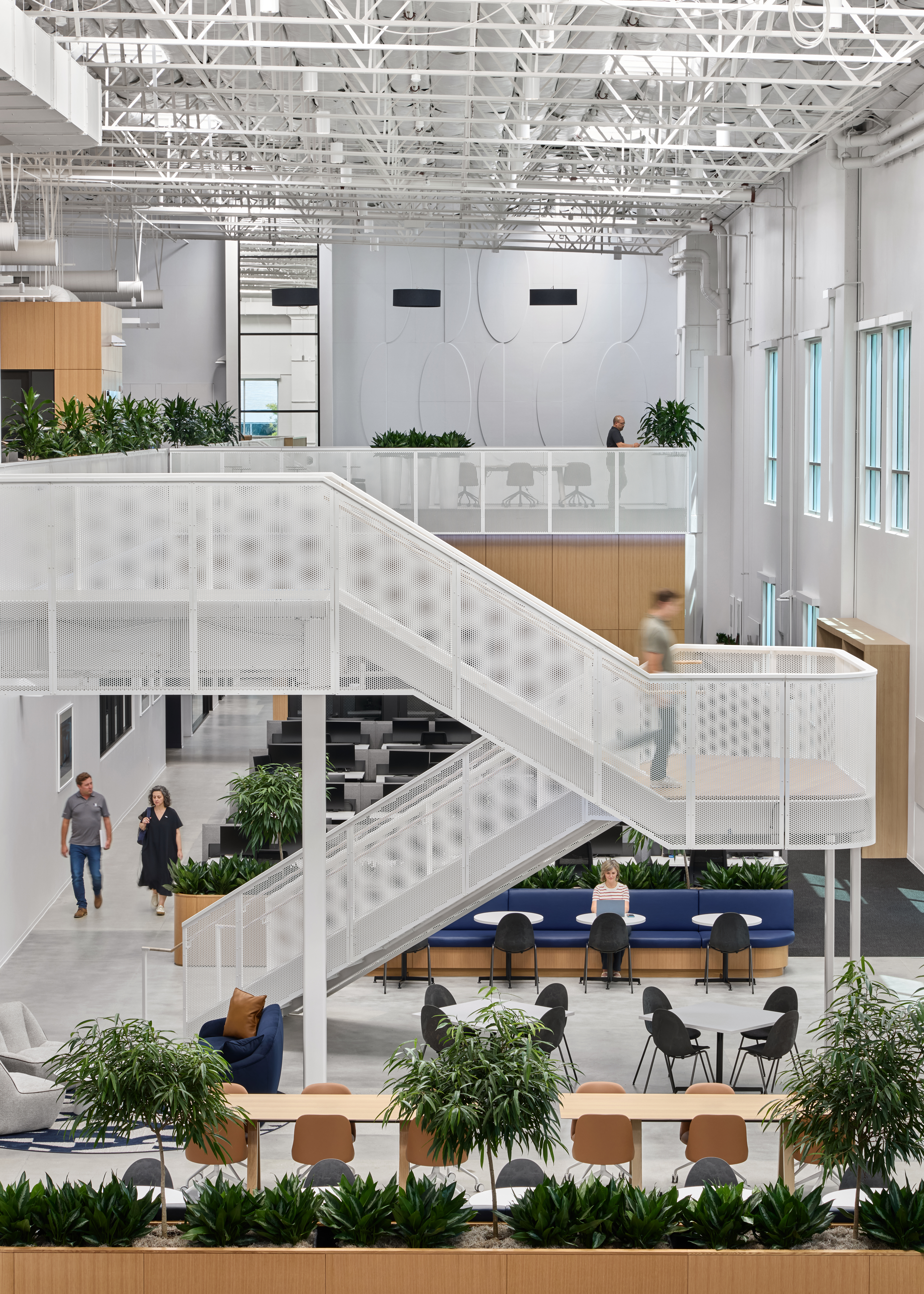 An architectural rendering of an office space with natural wood tones, white walls, open space, plant accents and a lot of natural light. A white, industrial-looking, multi-level staircase is the focus.